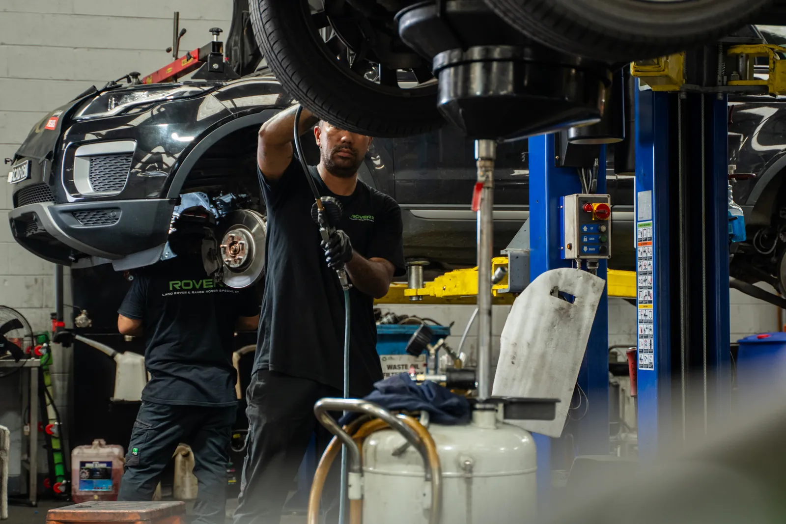 RoverX technicians inspecting suspension under a vehicle on the hoist